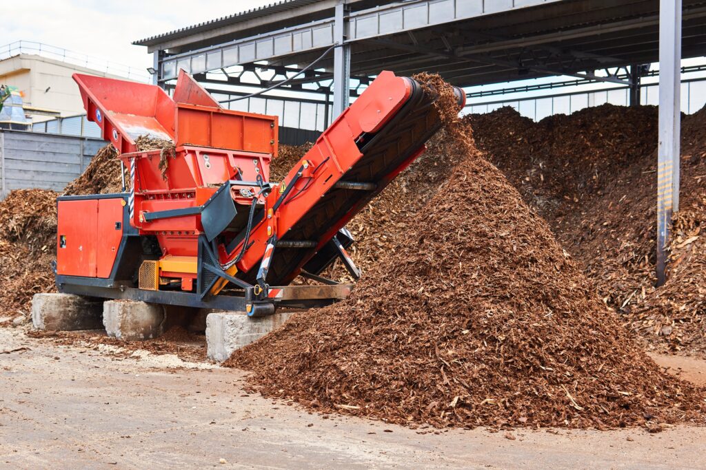 Forest byproduct like twigs and bark being processed into wood chips by an industrial wood shredder